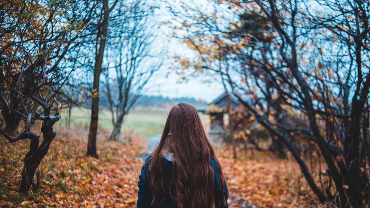 woman walking on dirt road beside bare trees